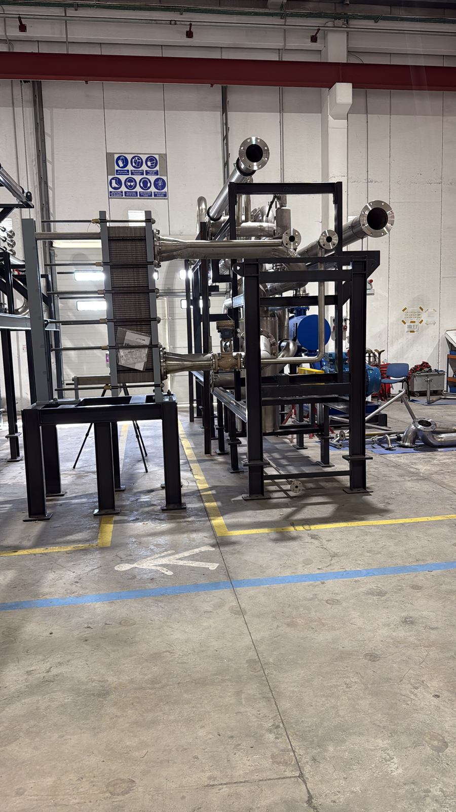 Skid industrial con tuberías de acero inoxidable, intercambiador de placas y bastidor metálico en un taller de calderería